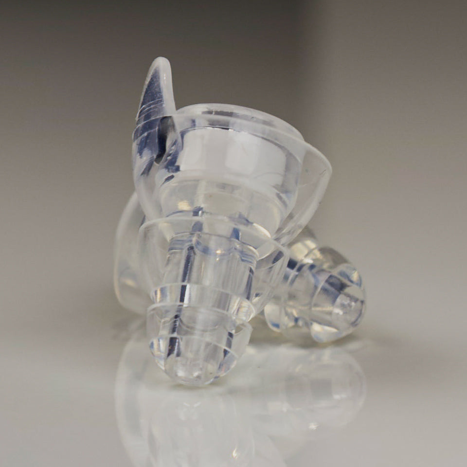 Clear plastic earbud on a reflective surface with a neutral background