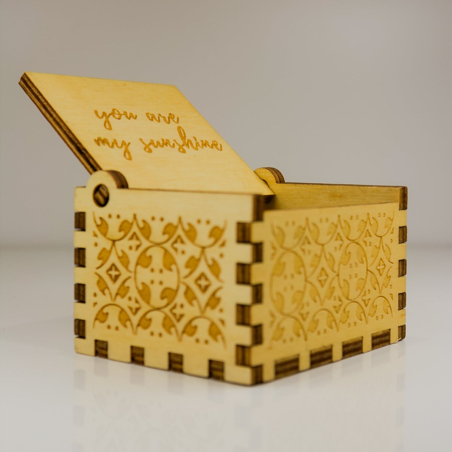 Wooden box with laser-cut patterns and 'you are my sunshine' text on a neutral background